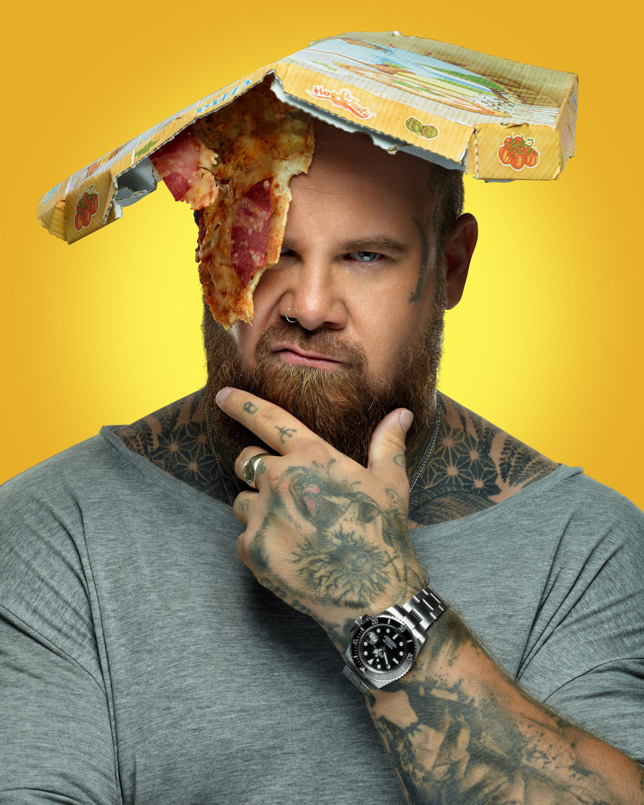 Der Tattoo-Artist Matti vom Fuchsbau in Freiburg. Mit Pizza über dem Auge und einem Pizzakarton auf dem Kopf im Studio abgelichtet für die Citylight-Kampange