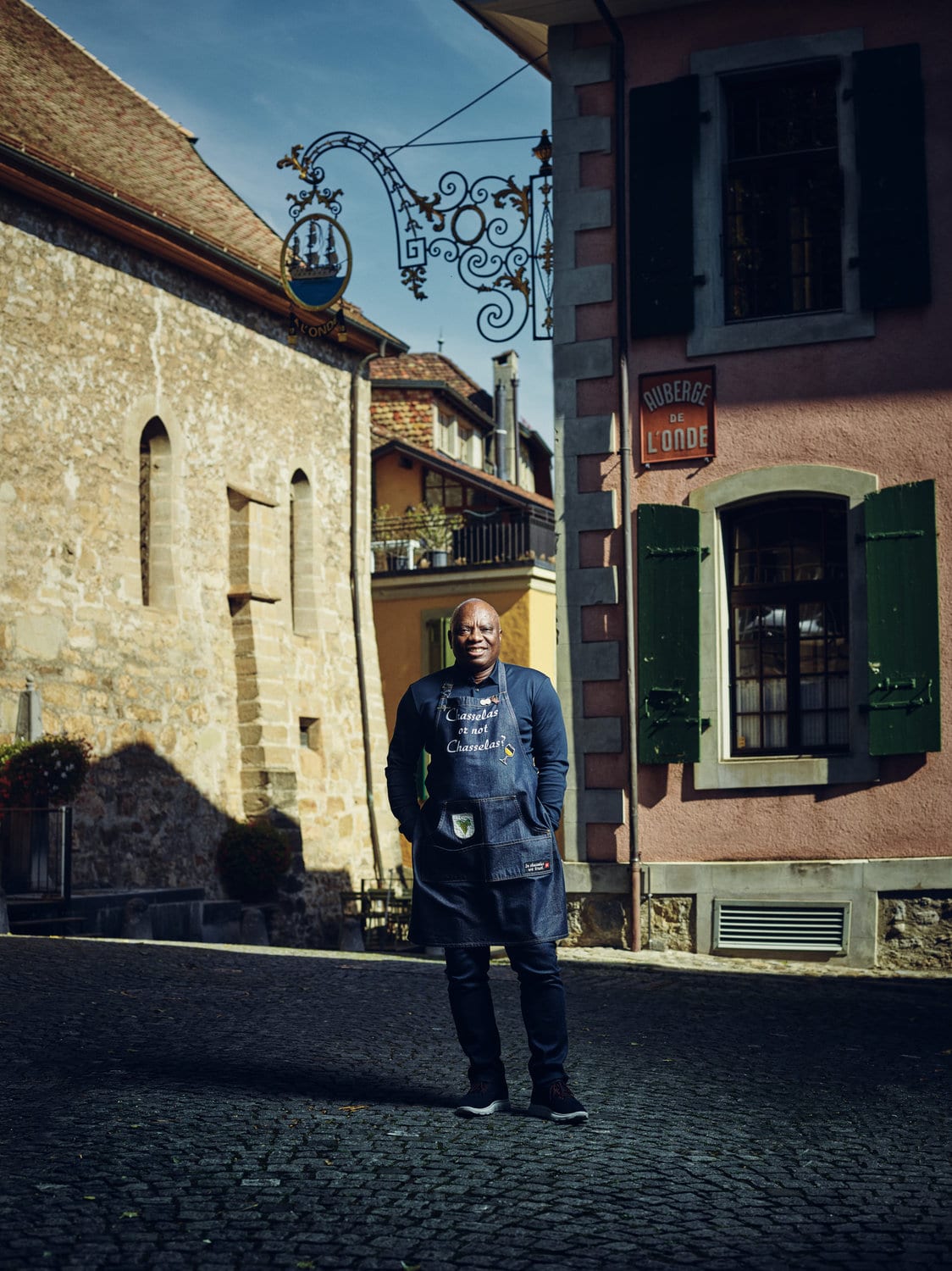 Jérôme Aké Béda vor der Auberge de l’Onde porträtiert mit seiner Schürze auf der steht. Chasselas or not Chasselas.