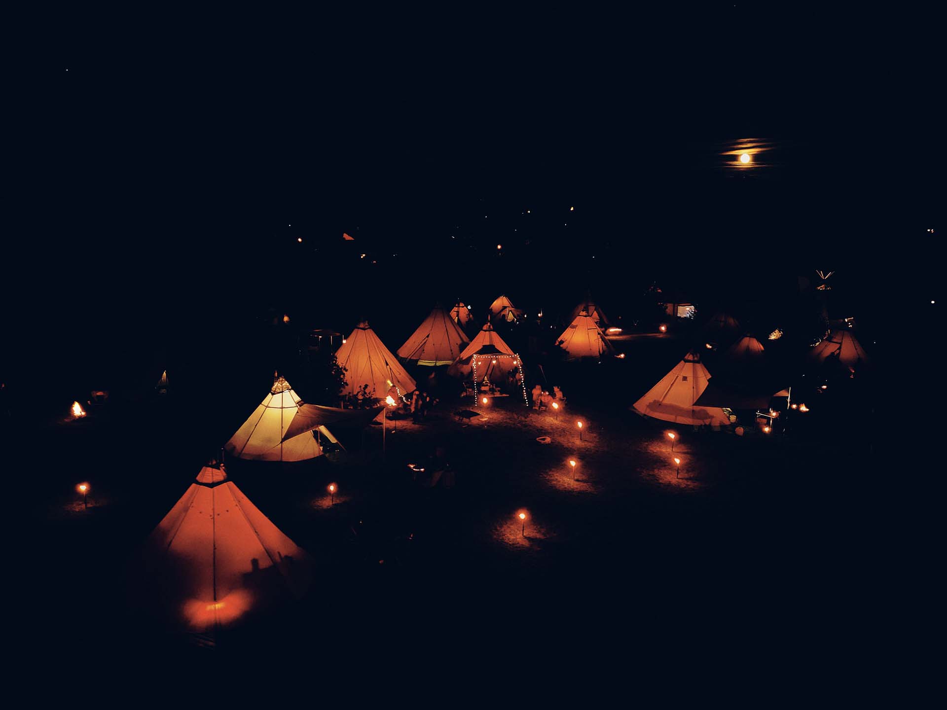 Nachtaufname aus der Luft des Tipicamps. Alle Zelte sind beleuchtet. Im Hintergrund scheint der Mond.