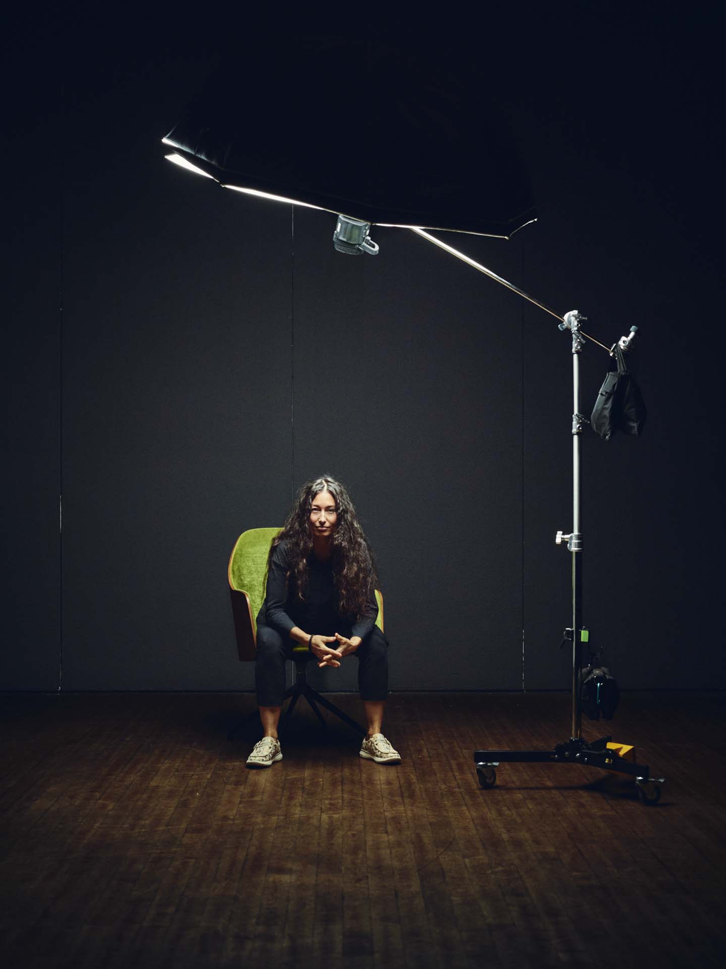 Studio-Portrait von Sydney Gessler, sitzend auf einem Stuhl unter einem großen Softlight. Die Aufnahme zeigt die Lichtquelle und den Aufbau, wodurch ein Blick hinter die Kulissen entsteht. Fotografiert von Felix Groteloh.